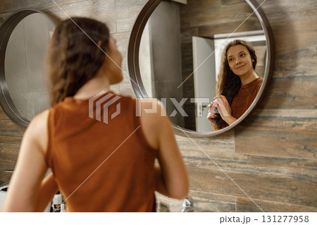 A woman reflects in a mirror while stylishly styling her hair in a modern bathroom 131277958