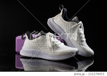 White sneakers rest elegantly on a smooth black surface combined with a vibrant purple block. The design emphasizes comfort and style ideal for various activities. 131278453