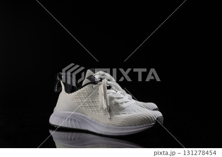 pair of white sneakers rests on a sleek black background showcasing their trendy design and comfortable style. Ideal for casual outings or workouts these shoes emphasize fashion and function. 131278454