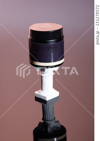 sleek cosmetics jar rests on an elegant pedestal showcasing beauty product design. The setting features a minimalistic background that highlights the product's sophisticated look. 131278572