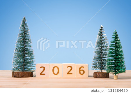 New Year 2026 and Christmas postcard. Wooden cubes with numbers 2026 and green Christmas trees on a wooden table and a blue background. 131284430