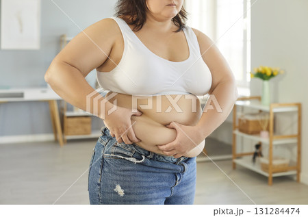 Unrecognizable overweight woman grabbing skin on her fat belly Unrecognizable overweight woman grabbing skin on her fat belly 131284474