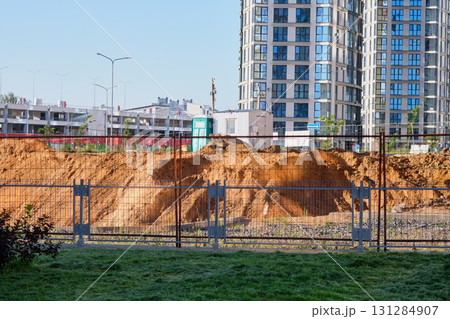 Heavy machinery operates on a construction site, revealing freshly dug earth behind safety barriers in a bustling urban landscape on a sunny day Heavy machinery operates on a construction site, revealing freshly dug earth behind safety barriers in a bustling urban landscape on a sunny day 131284907