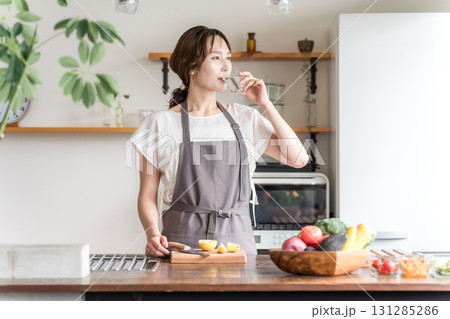 キッチンでコップで水を飲むエプロン姿の女性(水分補給,ミネラルウォーター,ウォーターサーバー) キッチンでコップで水を飲むエプロン姿の女性(水分補給,ミネラルウォーター,ウォーターサーバー) 131285286