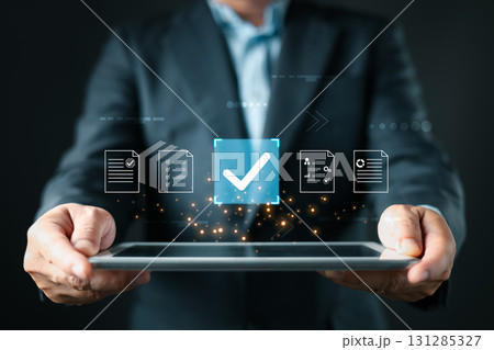A business professional holds a tablet displaying floating document icons, a large checkmark symbolizing digital approve processes, focusing on business quality assurance and data management. A business professional holds a tablet displaying floating document icons, a large checkmark symbolizing digital approve processes, focusing on business quality assurance and data management. 131285327