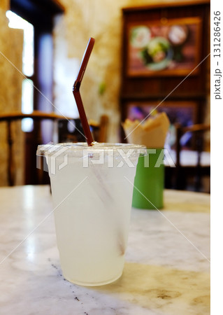 Cold lemonade juice with brown bulb in plastic glass on white table in cafe Cold lemonade juice with brown bulb in plastic glass on white table in cafe 131286426