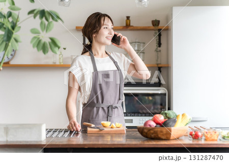 キッチンでスマホを使って電話・連絡・おしゃべりする主婦のアジア人女性（長電話） 131287470