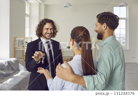 Young male realtor giving house key from new apartments to a happy smiling couple customers. 131288376