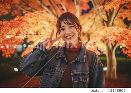 ライトアップされた紅葉の下でピースサインをする女性 131289054