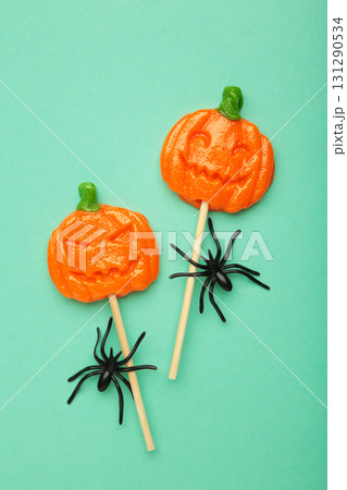 Halloween lollipops shaped like a pumpkin with decorative spider on mint background. Vertical photo 131290534