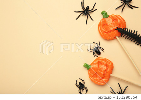 Halloween lollipops shaped like a pumpkin with decorative spider on beige background. 131290554