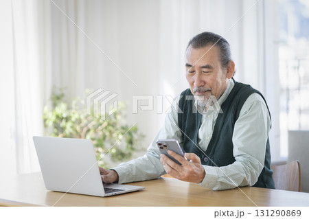 ノートパソコンで作業をしながらスマートフォンを見るシニア男性 131290869