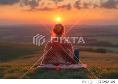 Woman sitting on hill watching warm sunset over valley landscape Woman sitting on hill watching warm sunset over valley landscape 131292189