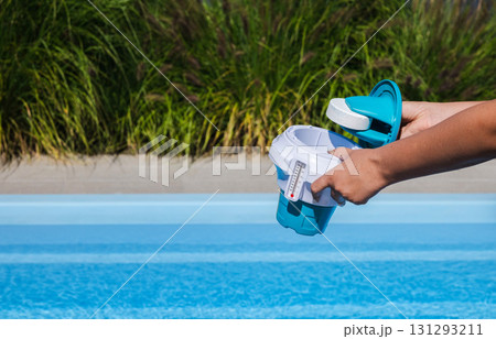 Hands placing chlorine tablet into pool dispenser for water disinfection and safe swimming 131293211