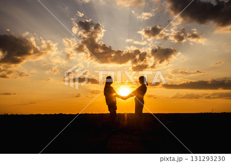 Two women standing in a field at sunset, holding hands in silhouette against the dramatic sky Two women standing in a field at sunset, holding hands in silhouette against the dramatic sky 131293230