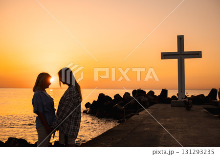 Two women holding hands at sunrise near a large cross monument by the sea in Varna, Bulgaria Two women holding hands at sunrise near a large cross monument by the sea in Varna, Bulgaria 131293235