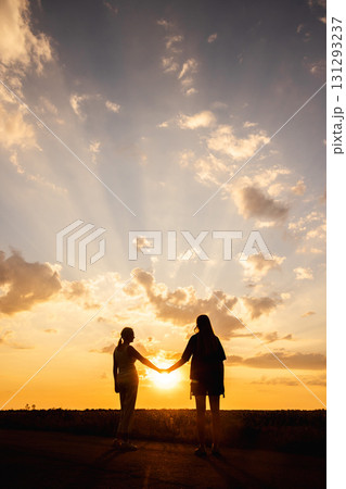Two women holding hands in silhouette at sunset with dramatic rays of light breaking through the clouds Two women holding hands in silhouette at sunset with dramatic rays of light breaking through the clouds 131293237