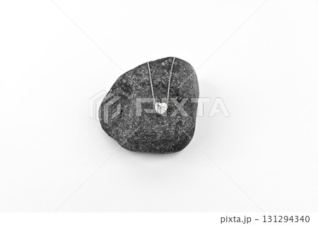 A heart shaped diamond pendant is sitting on a rock A heart shaped diamond pendant is sitting on a rock 131294340