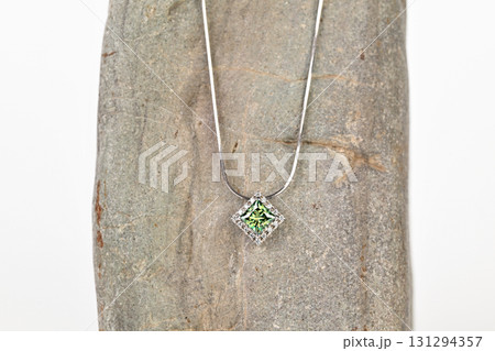 A green gemstone pendant is displayed on a rock 131294357