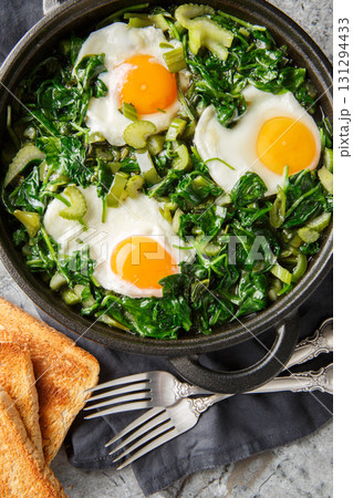 Healthy green shakshuka with eggs, spinach, celery, onion, green pepper and herbs close-up in a frying pan on the table. Vertical top view 131294433