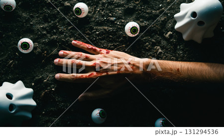 Bloody hand surrounded by plastic eyeballs and ghost figurines on dirt. 131294536