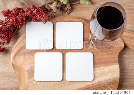 Flat lay product mockup with four blank square coasters on rustic wooden surface, styled with wineglass and berries, perfect for showcasing branding or sublimation designs. 131294907