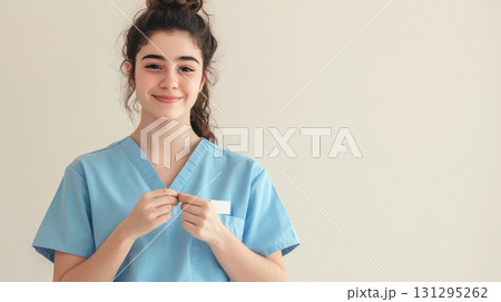 Minimalistic scene of healthcare worker in blue scrubs adding thank-you badge, expressing appreciation and professionalism, ideal for medical campaigns and recognition visuals. 131295262
