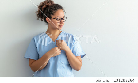 Emotive portrait of female nurse wearing medical uniform while attaching a small gratitude badge, captured in soft light with subtle pastel tones and calm, modern composition. 131295264