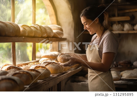 A candid shot of a female baker arranging loaves in a rustic bakery, ideal for branding warm, artisan food products and authentic small business imagery. A candid shot of a female baker arranging loaves in a rustic bakery, ideal for branding warm, artisan food products and authentic small business imagery. 131295895