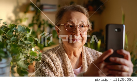 Senior woman creating vertical video content at home with smartphone and tripod, lifestyle setting for digital media and social platforms 131296086