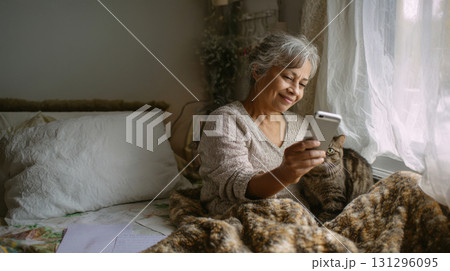 Grandma recording vertical advice video from bedroom with cat and soft light, cozy interior for real-life senior storytelling Grandma recording vertical advice video from bedroom with cat and soft light, cozy interior for real-life senior storytelling 131296095
