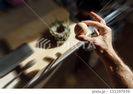 A chicken egg in a hand. A bird's nest in the table at the background. Kitchen interior.  131297039