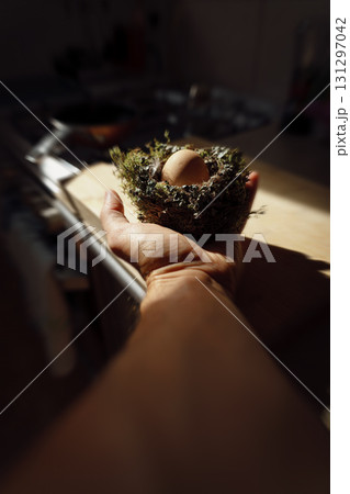 A man's hand holding a bird's nest with an egg inside, illuminated by the morning sun. A man's hand holding a bird's nest with an egg inside, illuminated by the morning sun. 131297042