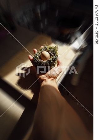 A man's hand holding a bird's nest with an egg inside, illuminated by the morning sun. A man's hand holding a bird's nest with an egg inside, illuminated by the morning sun. 131297043