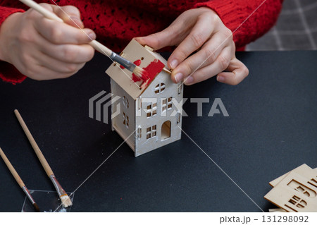 Sustainableminded Christmas cozy atmospheric festive decor in modern scandinavian home handmade decoration. Unrecognizable woman in red sweater painting craft wooden houses. Seasonal activity for kids Sustainableminded Christmas cozy atmospheric festive decor in modern scandinavian home handmade decoration. Unrecognizable woman in red sweater painting craft wooden houses. Seasonal activity for kids 131298092