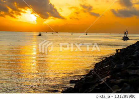 Tranquil dawn seascape. Beautiful sunrise over the sea, featuring traditional fishing boats catching the first light. Tranquil dawn seascape. Beautiful sunrise over the sea, featuring traditional fishing boats catching the first light. 131299980