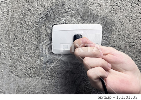 A smoking electrical outlet, a hand pulling the plug out of a burning outlet 131301335