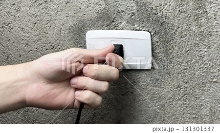 a hand pulling the plug out of an outlet a hand pulling the plug out of an outlet 131301337