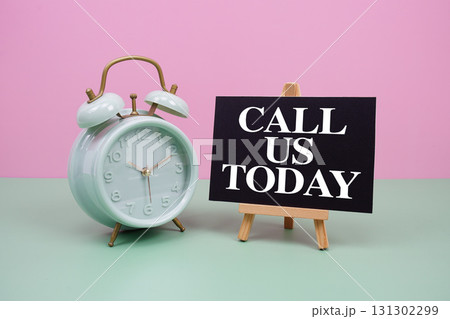 Call Us Today text with alarm clock on pink and green background 131302299
