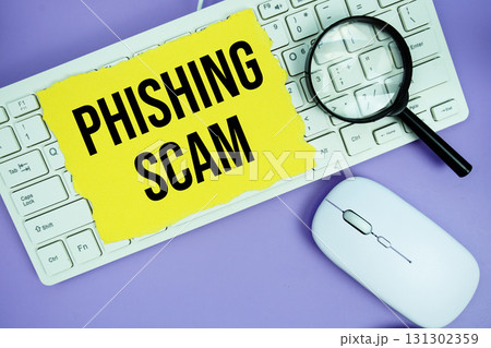 Yellow torn paper with the text "Phishing Scam" placed on a white keyboard, and magnifying glass and a computer mouse Yellow torn paper with the text "Phishing Scam" placed on a white keyboard, and magnifying glass and a computer mouse 131302359