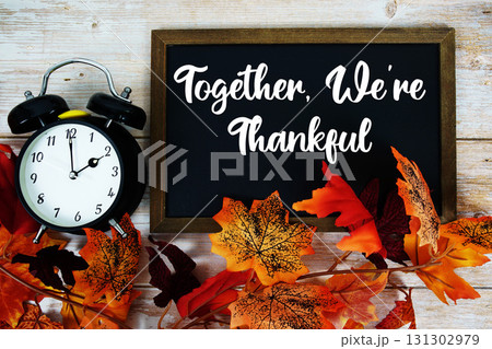 Together, We're Thankful text written on chalkboard with alarm clock and maple leaf decoration on wooden background 131302979