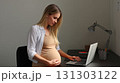 Happy pregnant mom working remotely on laptop. Online video call. Smiling and engaged, the pregnant mom showcases her multitasking skills during a video call. 131303122