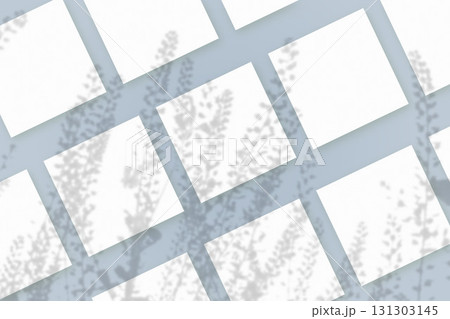 Natural light casts shadows from wildflowers on several sheets of white paper lying on a blue background. Mockup 131303145