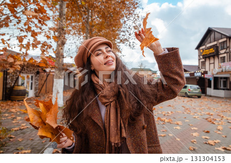 Autumn vibes and city stillness follow a fashionable young woman as she enjoys her weekend walk, breathing in the charm of golden leaves and urban elegance. 131304153