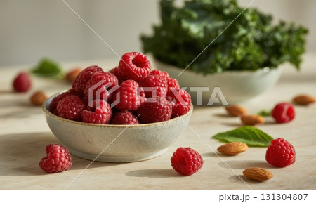 Light ceramic bowl overflowing with fresh, vibrant raspberries, almonds, and kale on a table 131304807