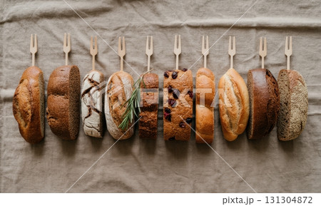 Assortment of artisanal bread slices and loaves with wooden forks on linen fabric Assortment of artisanal bread slices and loaves with wooden forks on linen fabric 131304872