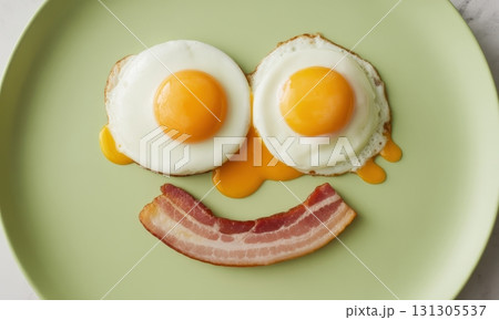 Sunny side up eggs and bacon strip arranged as a happy smiley face on a green plate 131305537