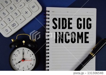 Side Gig Income text written on notepad with calculator and alarm clock on navy blue background 131306540