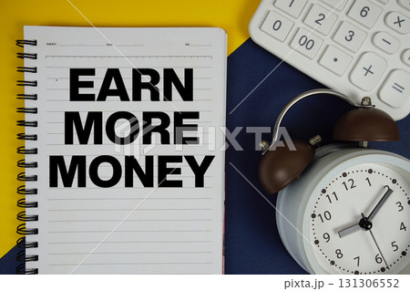 Earn More Money text written on notepad with calculator and alarm clock on navy blue background 131306552