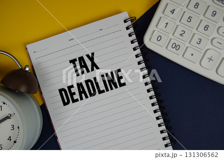 Tax Deadline text written on notepad with calculator and alarm clock on navy blue background 131306562